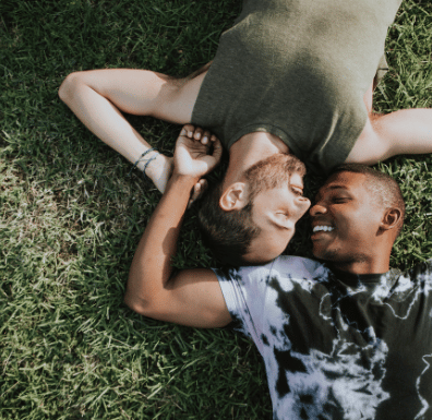 lgbtq couple laying in the grass looking at eachother.